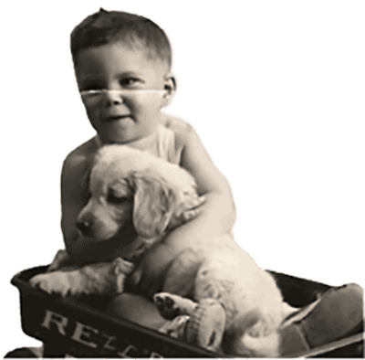 A black and white image of a young child in a diaper, smiling, seated in a small wagon and hugging a fluffy puppy. - 1 Minute Dog Training Book